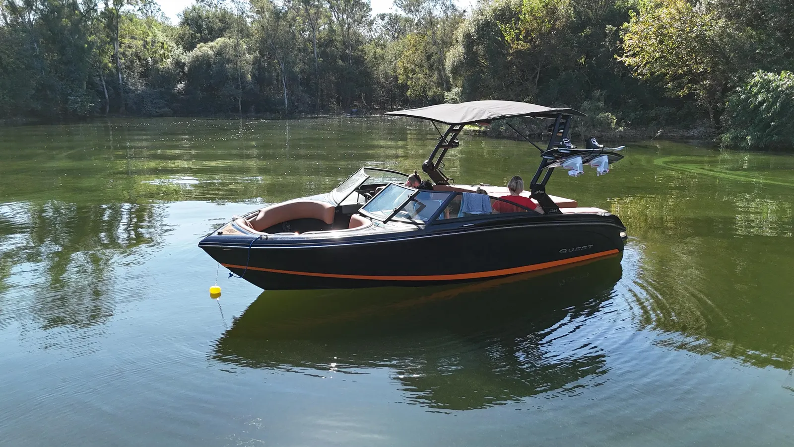 Lancha negra y naranja con torre DM Matrix y bimini, fondeada en un río de monte